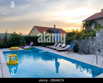 I lettini per il sole si trovano lungo le pareti in pietra accanto alla piscina nel giardino Foto Stock