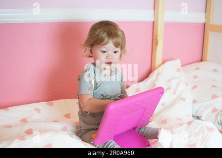 Carina ragazza caucasica toddler guardare tablet sul letto. Concetto di bambini e tecnologia Foto Stock