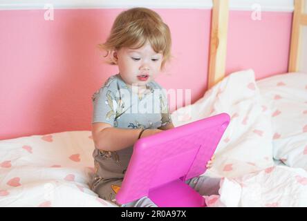 Carina ragazza caucasica toddler guardare tablet sul letto. Concetto di bambini e tecnologia Foto Stock