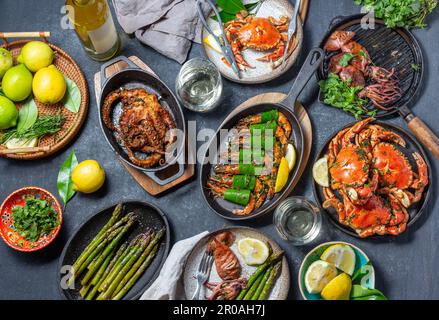 Set table con piatti di pesce - granchi cotti, gamberetti tigre, polpi alla griglia e calamari su padelle e piatti alla griglia in ghisa, vino bianco. Vista dall'alto Foto Stock
