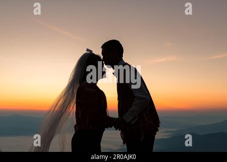 Silhouette di coppia di nozze in amore baciare e tenere la mano insieme durante l'alba con sfondo cielo mattina Foto Stock