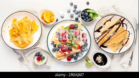 Varietà di crepes fresche con cioccolato, marmellata, frutta e frutti di bosco su sfondo bianco. Deliziose crepes fatte in casa. Vista dall'alto. Foto Stock