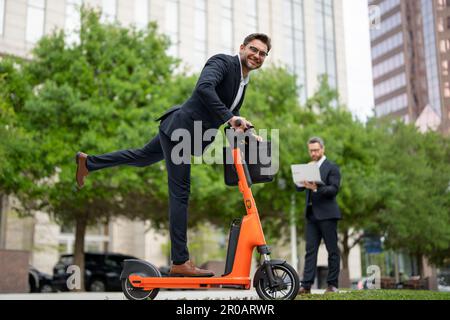 Business pazzo, veloce e facile. Uomo d'affari in tuta in sella a uno scooter elettrico in una riunione d'affari. Buon uomo d'affari con scooter all'aperto. Divertente Foto Stock