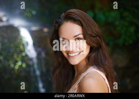 Le ceneri che si toccano con la natura. Ritratto di una bella giovane donna in piedi in una foresta con una cascata sullo sfondo. Foto Stock