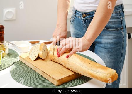 Vista in primo piano delle mani femminili che tagliano baguette fresche sulle fette Foto Stock