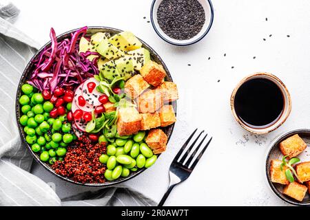 Cibo vegano sano. Ciotola di Buddha con quinoa, tofu fritto, avocado, edamame, piselli verdi, ravanello, cavolo e semi di sesamo. Backgroun tavolo da cucina bianco Foto Stock