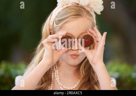 Aspetto dolce. Una bambina che tiene playfully i cupcakes davanti ai suoi occhi. Foto Stock