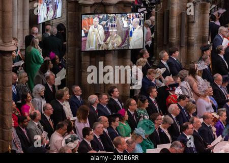 Gli ospiti e i membri della congregazione osservano i rituali di incoronazione sugli schermi all'interno dell'Abbazia di Westminster del Re Carlo III e della Regina Consorte. Foto Stock