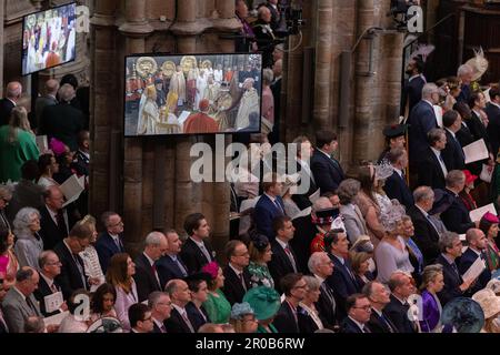 Gli ospiti e i membri della congregazione osservano i rituali di incoronazione sugli schermi all'interno dell'Abbazia di Westminster del Re Carlo III e della Regina Consorte. Foto Stock