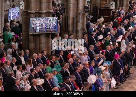 Gli ospiti e i membri della congregazione osservano i rituali di incoronazione sugli schermi all'interno dell'Abbazia di Westminster del Re Carlo III e della Regina Consorte. Foto Stock