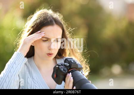 Preoccupato fotografo che controlla le foto difettose su una macchina fotografica mirrorless in un parco Foto Stock