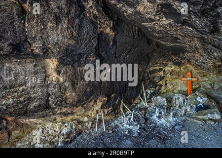 In una grotta lungo il sentiero per il santuario della Santa trinità una croce arancione e candele accese da devoti pellegrini. Vallepietra, provincia di Roma, Lazio Foto Stock