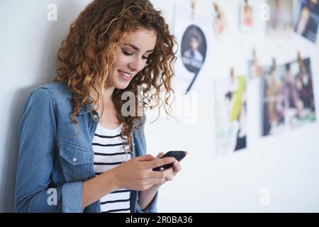 Prendersi cura di alcuni testi di lavoro. una giovane donna che usa un cellulare mentre si trova in ufficio. Foto Stock