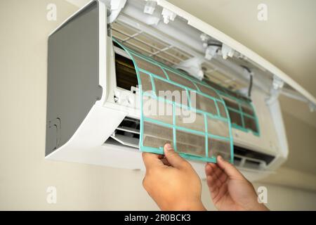 Tecnico professionista maschile che ripara un elettricista ripara un condizionatore d'aria all'interno. rimozione del filtro dell'aria riparazione delle temperature elevate Foto Stock