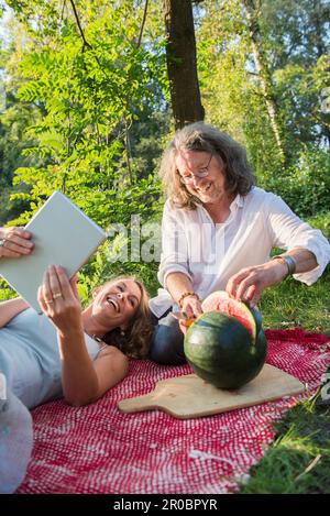 Coppia al pic-nic utilizzando tablet e il cocomero da taglio, Baviera, Germania Foto Stock
