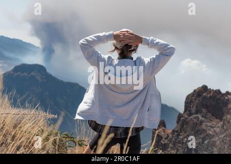 Ragazza turistica che guarda l'eruzione vulcanica di Cumbre Vieja sull'isola di la Palma, Isole Canarie. Vulcano la Palma da lontano vista aerea. Foto Stock
