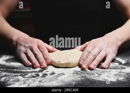 L'uomo capo del panettiere lavora l'impasto sul tavolo con la farina Foto Stock