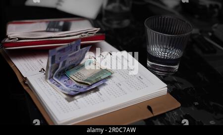 Rupia indiana piegato su un libro di note spianatore mensile aperto su un tavolo con mezzo bicchiere d'acqua e un portafoglio dietro di esso Foto Stock