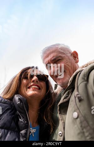 felice coppia di mezza età che prende un selfie di fronte a un dinosauro in un parco pubblico - vacanza e concetto di stile di vita di viaggio Foto Stock