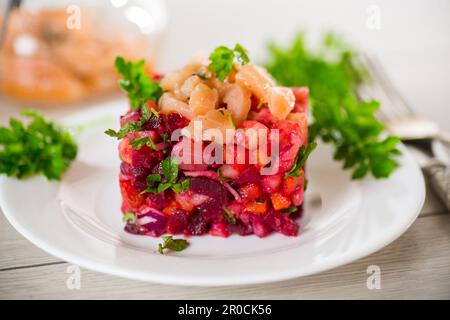 insalata di vinaigrette di verdure bollite con pesce salato in un piatto, su un tavolo di legno. Foto Stock