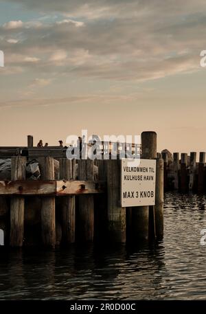 Un'immagine verticale di un molo di legno intemperiato che si aggetta in un tranquillo corpo blu d'acqua Foto Stock
