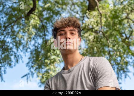 Angolo basso di un giovane, serio, guardando la telecamera in un parco pubblico Foto Stock