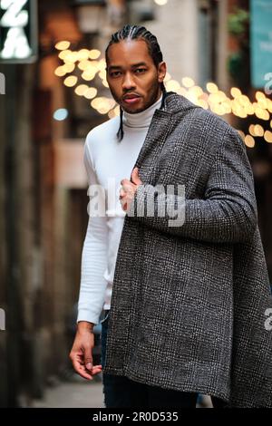 Elegante uomo afroamericano che guarda la fotocamera con il viso serio mentre indossa un cappotto in piedi all'aperto. Foto Stock