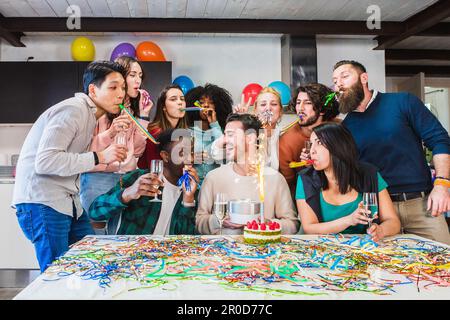 Amici felici che celebrano il compleanno del ragazzo, torta con candela fuochi d'artificio, umore festivo e risate nel salotto del ragazzo di compleanno. Filtro luminoso Foto Stock