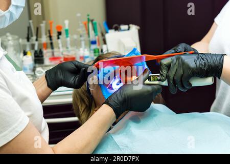 Ripristino della superficie di masticazione con materiale di riempimento in fotopolimero. Dentista che lavora con la lampada UV di polimerizzazione dentale in cavità orale Foto Stock