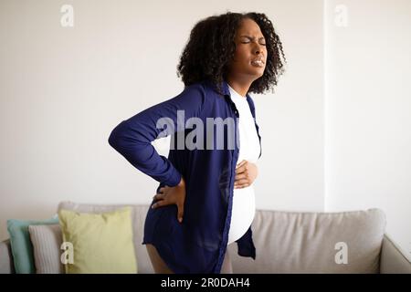 Donna incinta afroamericana disappaiata e infelice con grande pancia che soffre di mal di schiena Foto Stock