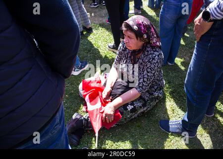 Izmir, Konak, Turchia 04.30.2023 una vecchia donna turca è stanca delle celebrazioni e seduta sull'erba con la sua bandiera turca Foto Stock