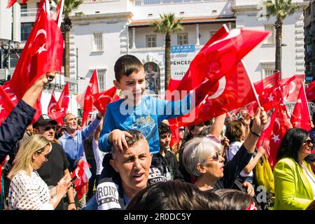 Izmir, Konak, Turchia 04.30.2023 Un ragazzo turco dai capelli neri con una camicia blu, seduto sulla spalla di suo padre, sventolando la bandiera turca, gente affollata Foto Stock