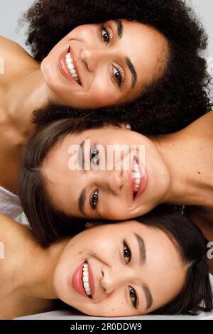Giovani tre donne diverse con una perfetta pelle del viso incandescente che si posa insieme e sorridente, verticale studio shot, primo piano Foto Stock