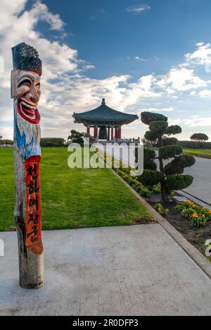 Uno splendido paesaggio della Campana dell'amicizia coreana in un lussureggiante parco verde con una colorata statua di palo in primo piano Foto Stock