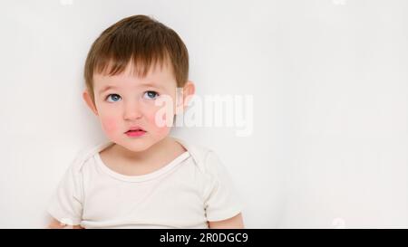 Il bambino attento guarda in su, sfondo bianco studio. Bambino triste con l'emozione del dubbio sul suo volto. Bambino di circa due anni (un anno nove mesi) Foto Stock