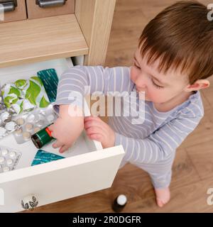 Il bambino del bambino ha aperto il cassetto dell'armadietto con le pillole e la medicina. Bambino che tiene una confezione di pillole nel salotto di casa. Bambino di età un anno nove mese Foto Stock