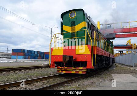 Locomotiva diesel che tira il treno merci caricato con container di carico presso il deposito di una stazione ferroviaria. Kiev, Ucraina. Foto Stock