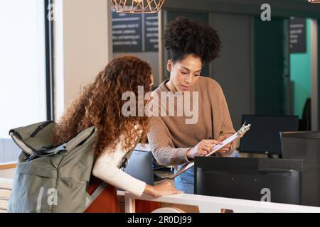 Giovane donna effettua il check-in alla reception, alla reception, all'hotel, all'ingresso alla biblioteca universitaria Foto Stock