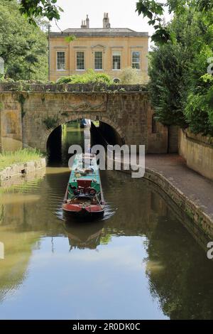 Una barca verde e rossa sul canale che passa sotto un ponte nei Sydney Gardens, Bath Foto Stock