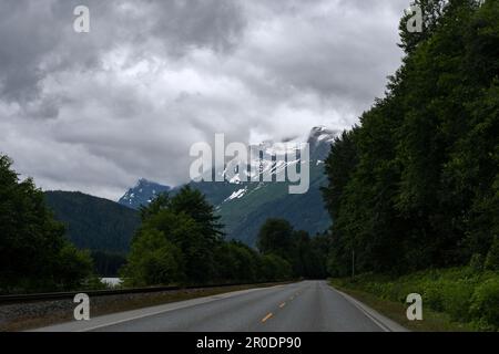 Una vista panoramica della campagna, caratterizzata da una strada asfaltata che conduce attraverso un paesaggio collinare con torreggianti montagne sullo sfondo Foto Stock