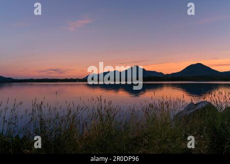 Una pittoresca scena di due maestose montagne che si affacciano su uno splendido cielo del tramonto, con un tranquillo lago in primo piano Foto Stock