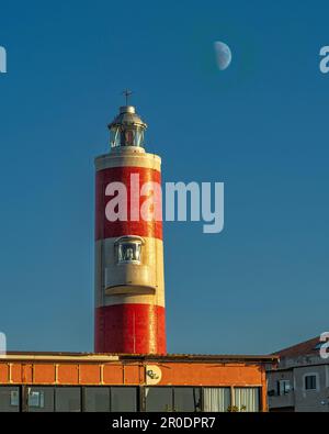 Faro di Punta pezzo a strisce rosse e bianche illuminato dal tramonto con la luna sullo sfondo. Villa San Giovanni, Calabria Foto Stock