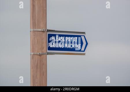 Un cartello per favore paga al parcheggio su un palo di legno presso un parcheggio auto Foto Stock