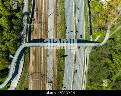 Ponte pedonale e pista ciclabile che unisce due parchi pubblici su binari ferroviari e autostrade cittadine a più corsie a Cracovia, Polonia Foto Stock