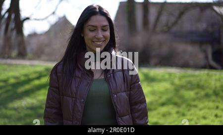 Una giovane donna passa attraverso il parco con un sorriso spensierato sul viso, godendosi il sole e l'aria fresca Foto Stock