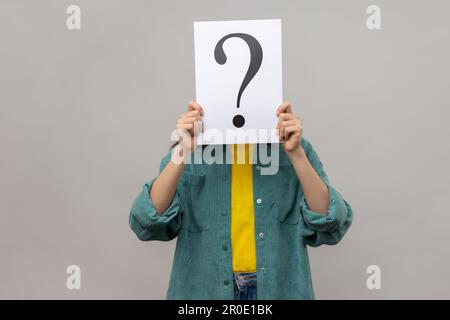 Ritratto di donna sconosciuta che copre il viso con punto interrogativo, trovare soluzione intelligente, chiedere consiglio, indossare giacca casual stile. Studio in interni isolato su sfondo grigio. Foto Stock