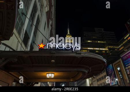 Vista notturna dell'esterno del cartello di Macy sulla parete del negozio con l'Empire state Building sullo sfondo tra i grattacieli. New York, Manhattan, Stati Uniti. Foto Stock