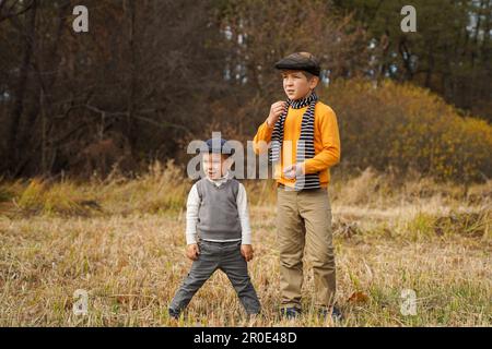 Due simpatici ragazzi in abiti retrò in posa in un campo estivo e guardando in lontananza Foto Stock