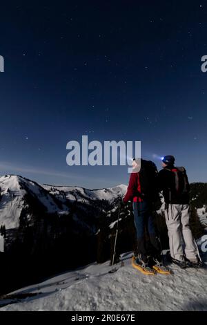 Escursionisti con racchette da neve al chiaro di luna sulla cima vicino Bolsterlang a Allgäu, Germania Foto Stock