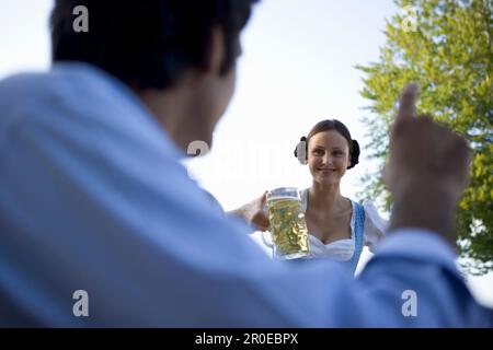 Cameriera che serve birra stein a un giovane nella birreria all'aperto di Monaco, Baviera Foto Stock